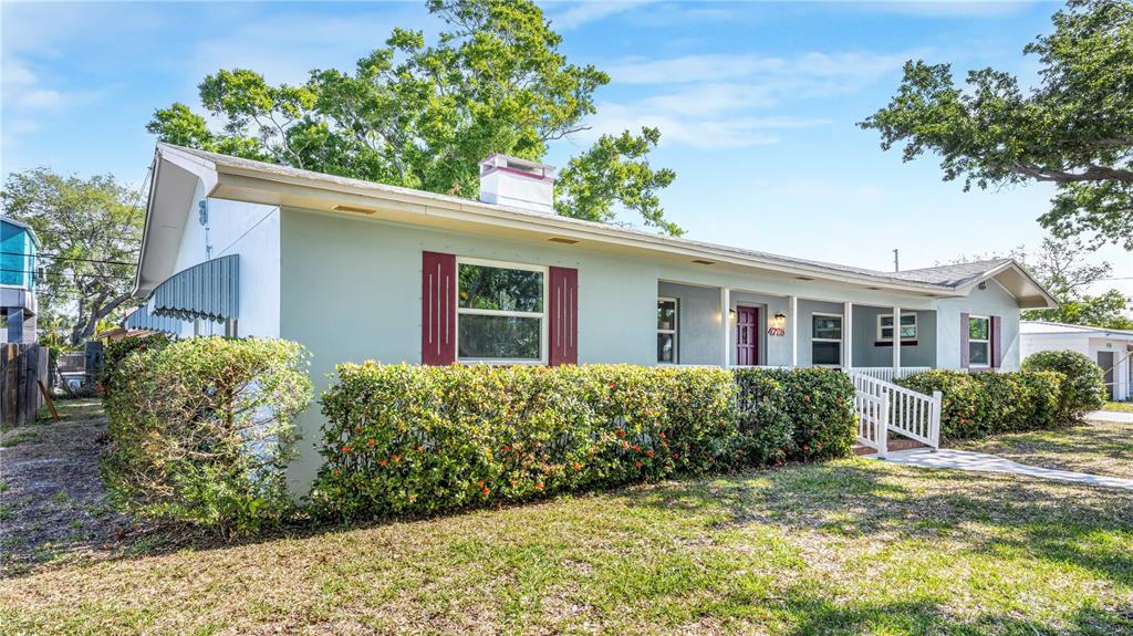 A light green single-story house features a red-trimmed window, a covered porch, and landscaping — 4725 DEL RIO WAY S, GULFPORT, FL