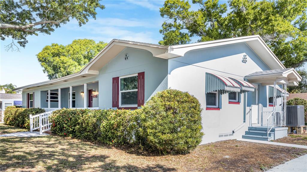 A light blue single-story house with a covered porch, red shutters, and green landscaping — 4725 DEL RIO WAY S, GULFPORT, FL