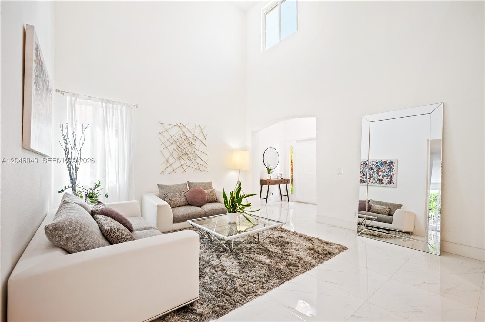 A bright living room features high ceilings, white tile floors, and a large floor mirror — 445 Conservation Dr, Weston FL 33327, WESTON, FL