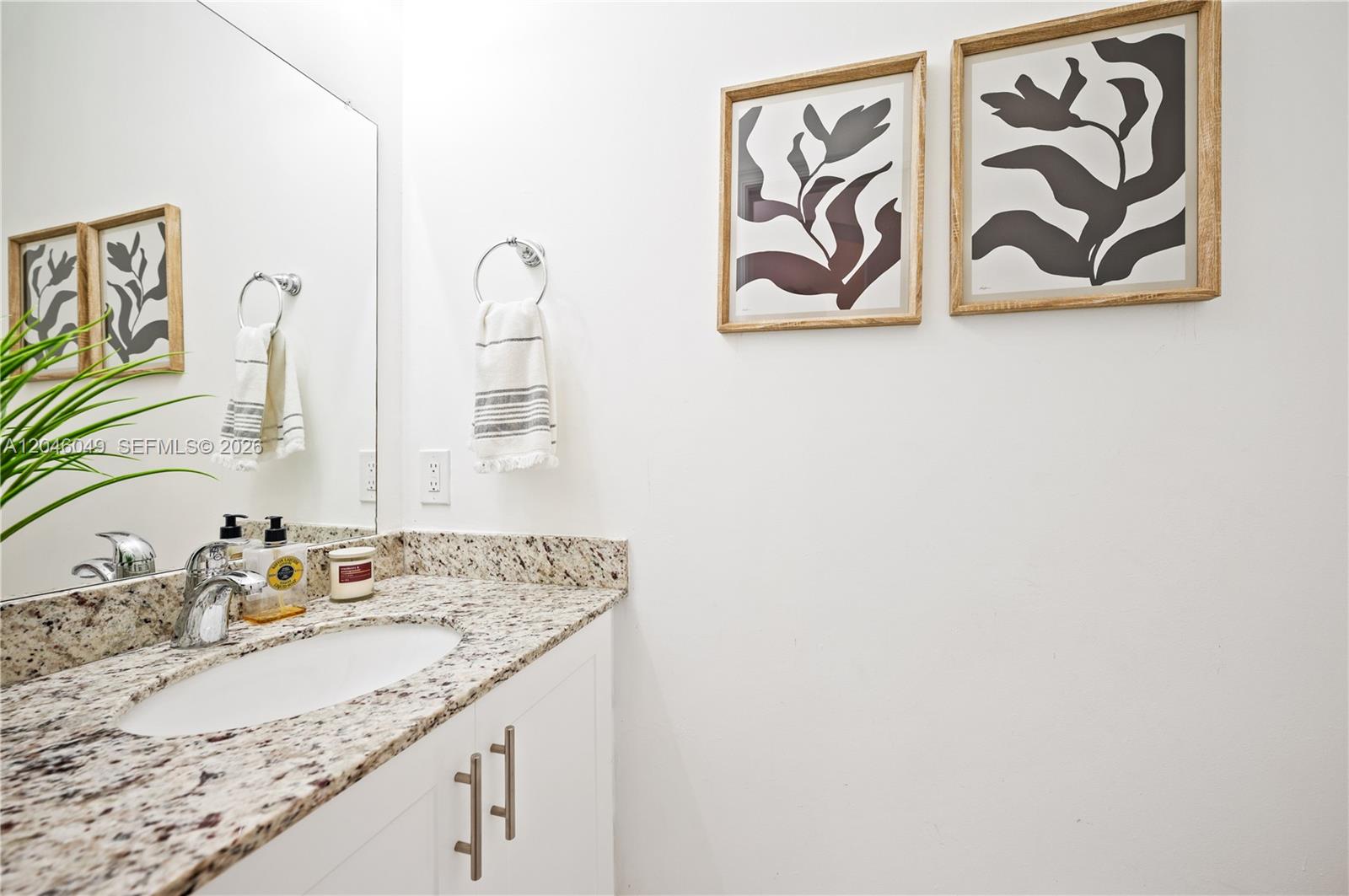 A bathroom features a granite vanity countertop, a white cabinet, and two framed botanical prints — 445 Conservation Dr, Weston FL 33327, WESTON, FL