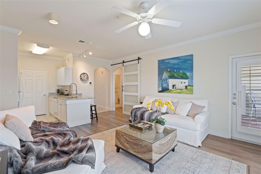 A living room with white sofas, a glass coffee table, and an open kitchen area — 1216 S MISSOURI AVENUE UNIT 419, CLEARWATER, FL