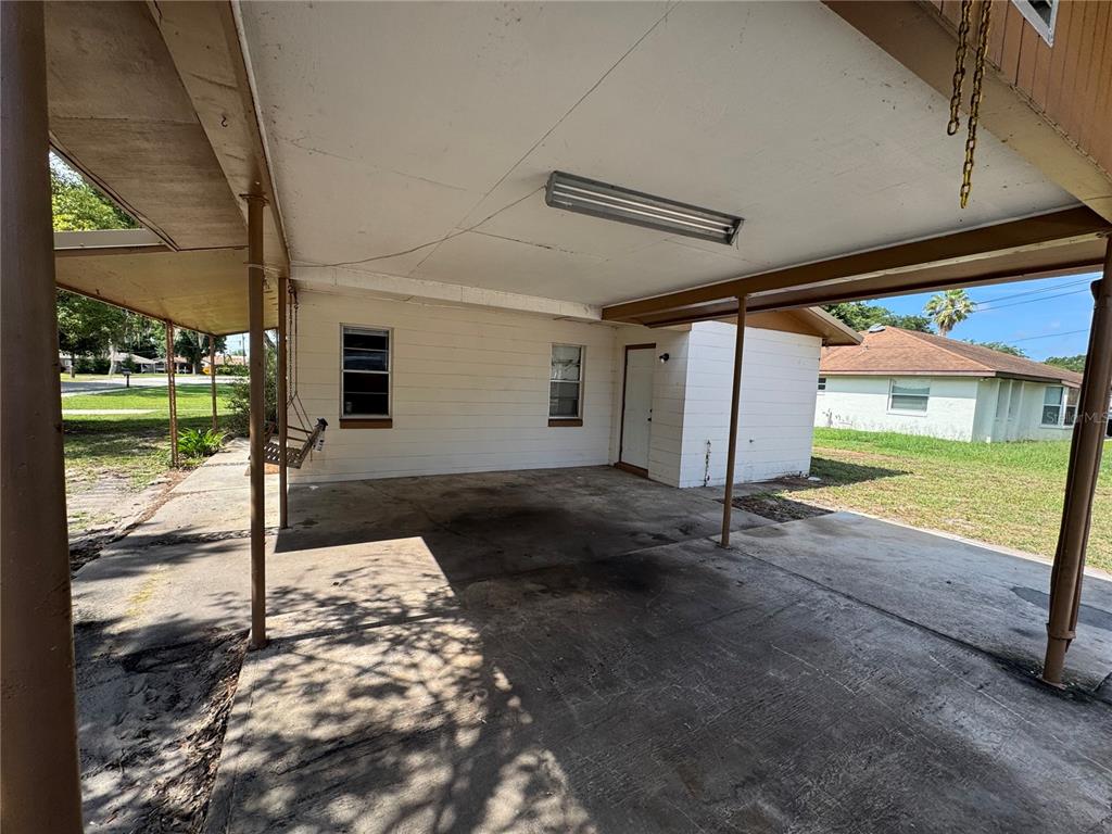 A covered concrete carport features a white exterior wall, two windows, and a hanging bench — 307 N LAKE REEDY BOULEVARD, FROSTPROOF, FL