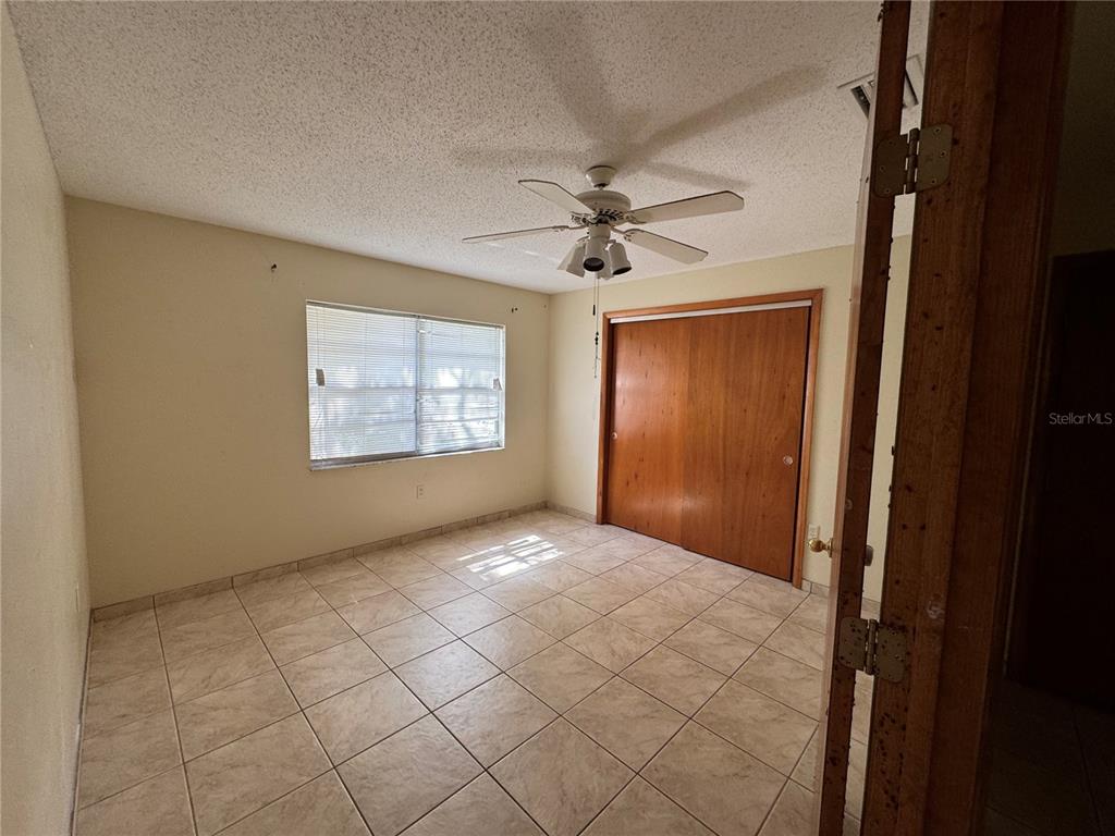 A bedroom features light-colored tile flooring, a ceiling fan, a window, and wood-paneled closet doors — 307 N LAKE REEDY BOULEVARD, FROSTPROOF, FL