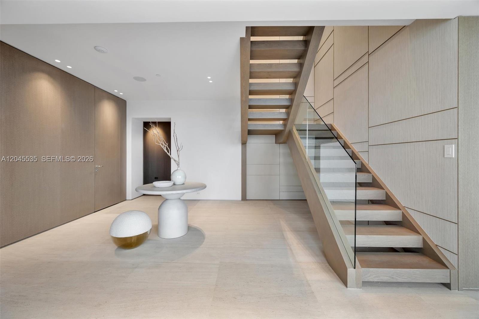 A modern entryway features a floating staircase, light wood paneling, and a minimalist pedestal table — 1100 Biscayne Blvd # 3906, Miami FL 33132, MIAMI, FL