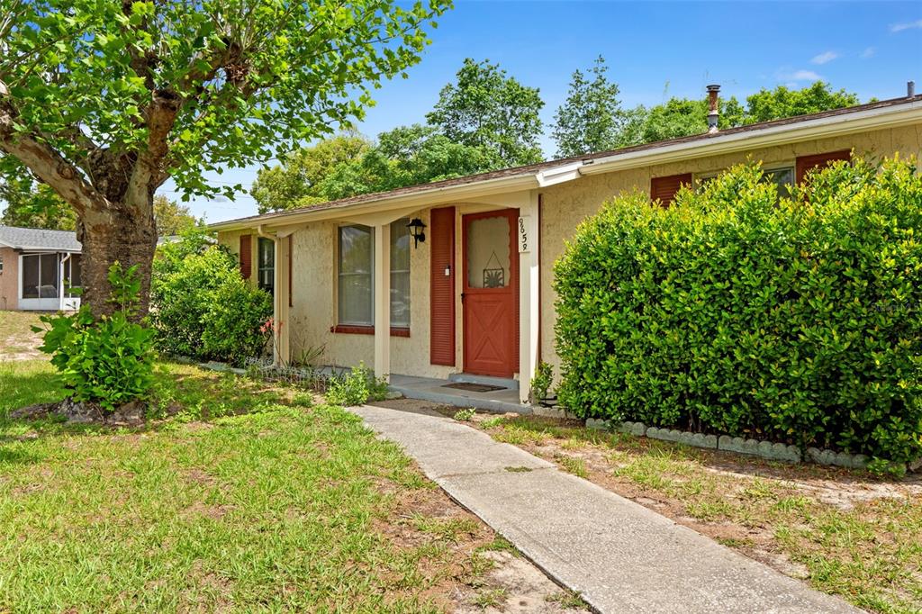A single-story house with a beige stucco exterior, red shutters, and a concrete walkway — 9658 BAYSIDE COURT, SPRING HILL, FL