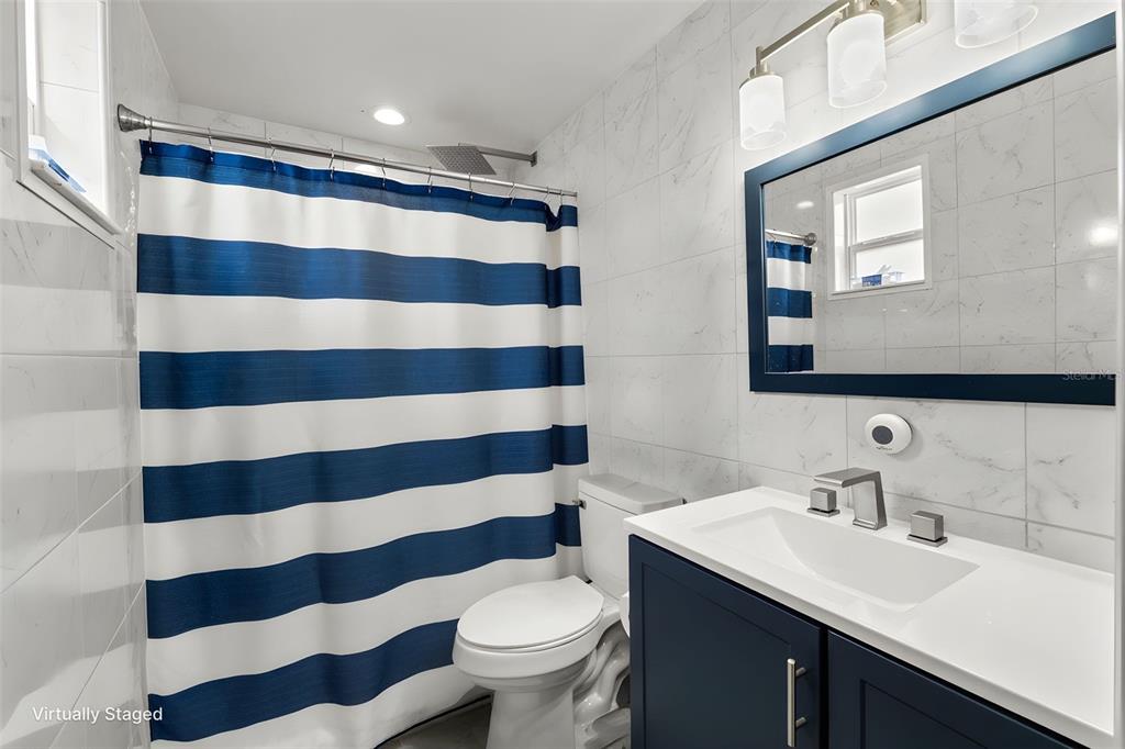 A bathroom features a blue and white striped shower curtain, marble-look tiles, and a vanity — 9658 BAYSIDE COURT, SPRING HILL, FL