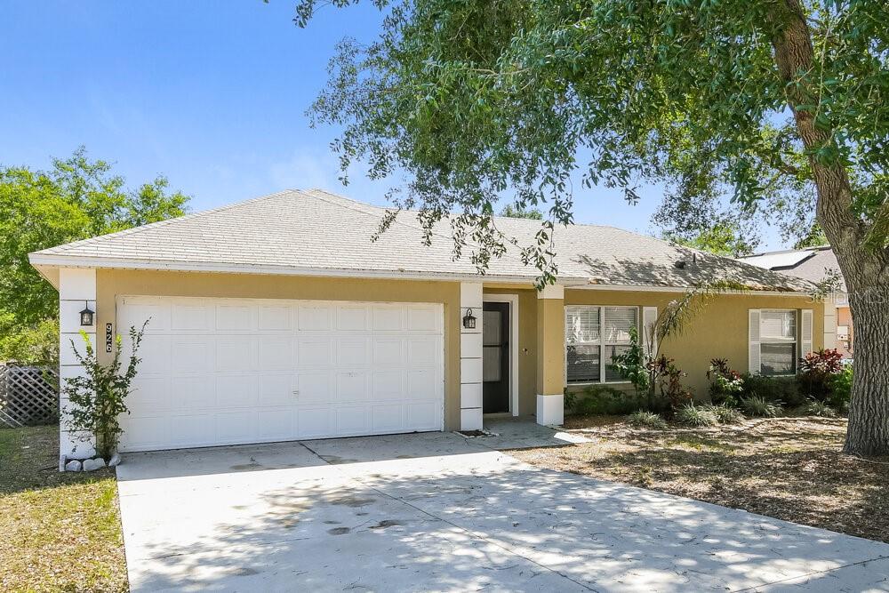 A single-story house with a white garage door, tan stucco exterior, and a concrete driveway — 926 WILLOW RUN STREET, MINNEOLA, FL
