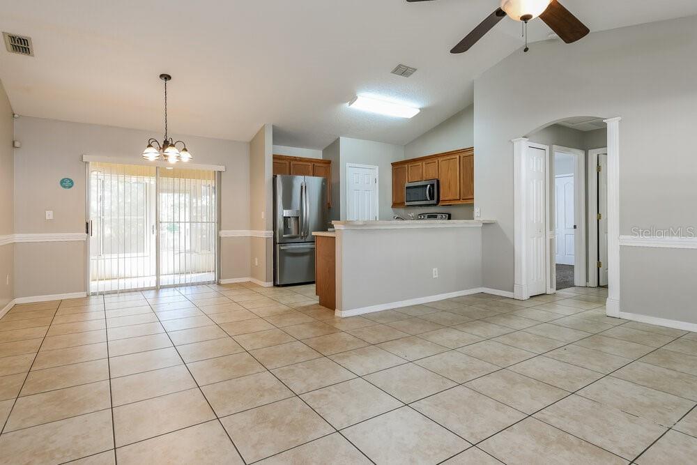 An open-concept kitchen and dining area features tile flooring, wood cabinets, and sliding glass doors — 926 WILLOW RUN STREET, MINNEOLA, FL