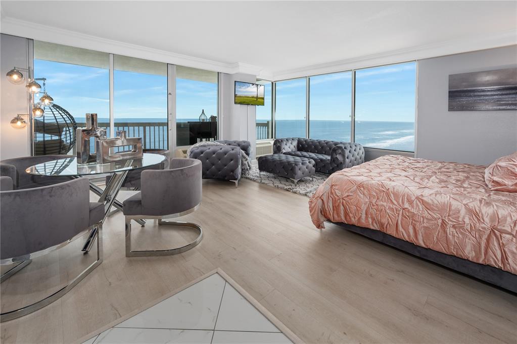 A bedroom with a dining area, gray tufted furniture, and floor-to-ceiling windows overlooking the ocean — 2700 N ATLANTIC AVENUE UNIT 1210, DAYTONA BEACH, FL