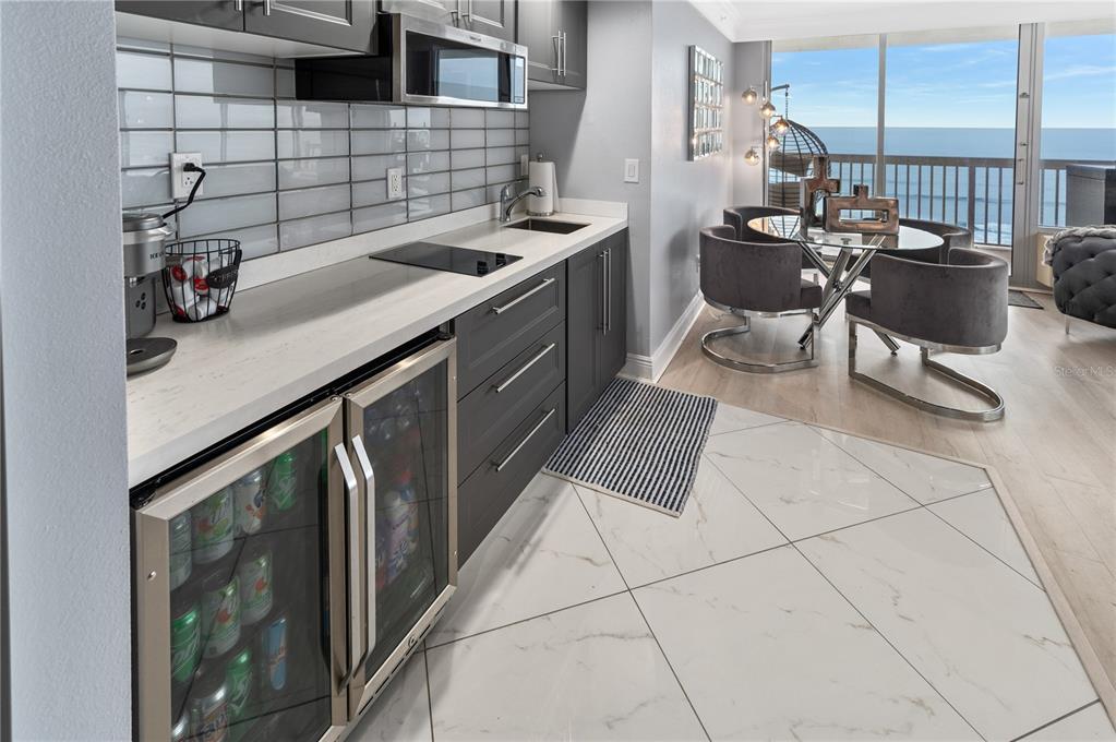 A modern kitchen features dark gray cabinetry, a beverage cooler, and a dining area overlooking the ocean — 2700 N ATLANTIC AVENUE UNIT 1210, DAYTONA BEACH, FL