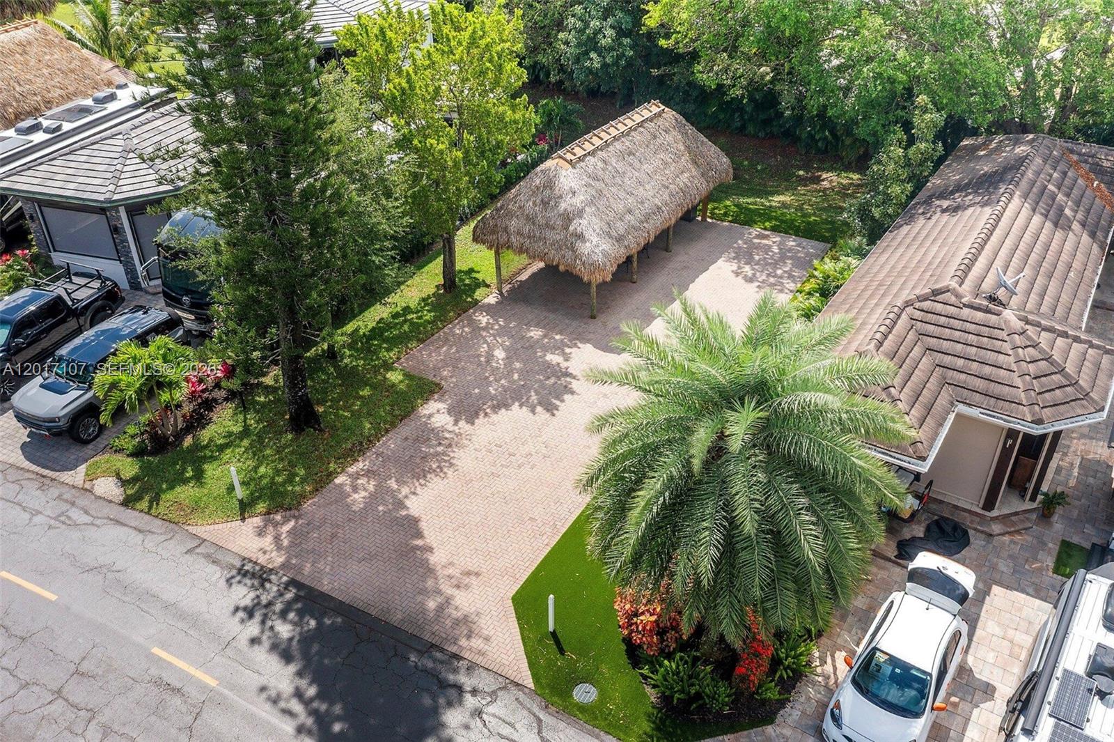 An aerial view shows a paved driveway with a thatched-roof structure and parked vehicles — 22 S Cortez Dr, Margate FL 33068, MARGATE, FL