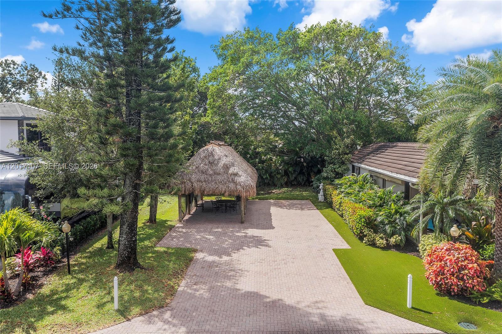 A paved patio area features a thatched-roof tiki hut surrounded by trees and landscaping — 22 S Cortez Dr, Margate FL 33068, MARGATE, FL