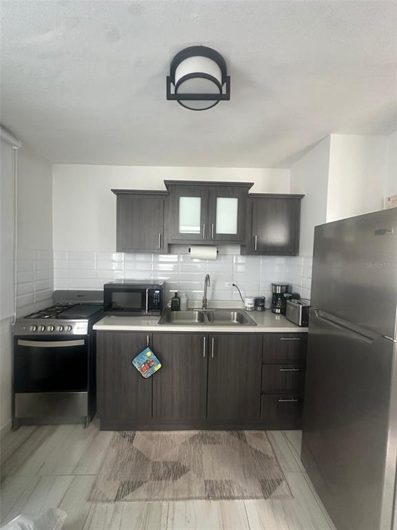 A kitchen features dark wood cabinets, stainless steel appliances, and a white subway tile backsplash — F14, 5013 Calle Colosense URB. EXTENSIÓN ELIZABETH, CABO ROJO, PR