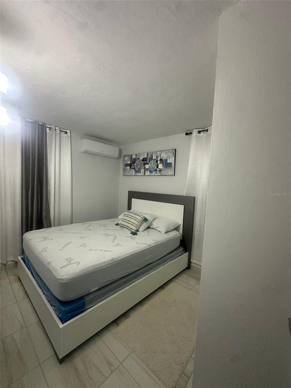 A bedroom features a bed with a white frame, tiled floors, and a wall-mounted air conditioner — F14, 5013 Calle Colosense URB. EXTENSIÓN ELIZABETH, CABO ROJO, PR
