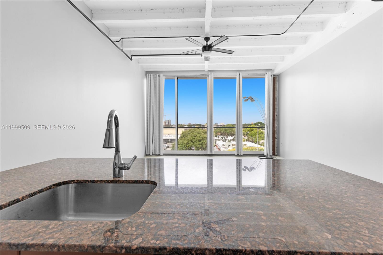A kitchen island with a granite countertop and sink overlooks a room with floor-to-ceiling windows — 8101 Biscayne Blvd # 414, Miami FL 33138, MIAMI, FL