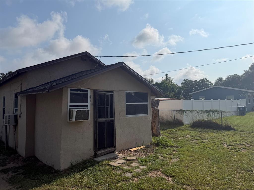 A small, beige, single-story house with a screen door and window air conditioning units — 114 W MURPHY STREET, DAVENPORT, FL