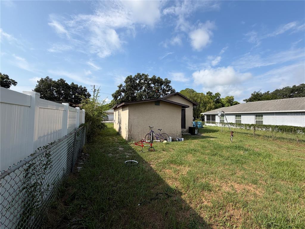 A small, tan-colored detached building sits in a grassy backyard next to a white fence — 114 W MURPHY STREET, DAVENPORT, FL
