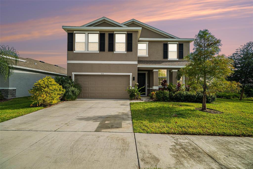 A two-story suburban house with a tan stucco exterior, a two-car garage, and a lawn — 5430 THISTLE FIELD COURT, WESLEY CHAPEL, FL