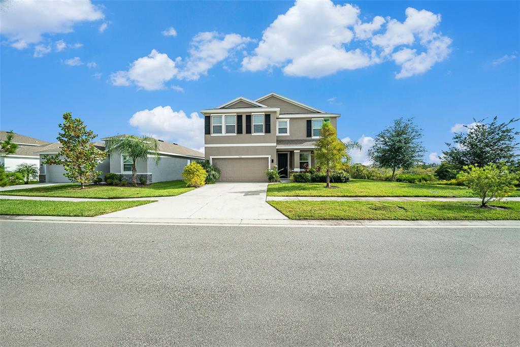 A two-story suburban house with a beige exterior, a two-car garage, and a front lawn — 5430 THISTLE FIELD COURT, WESLEY CHAPEL, FL