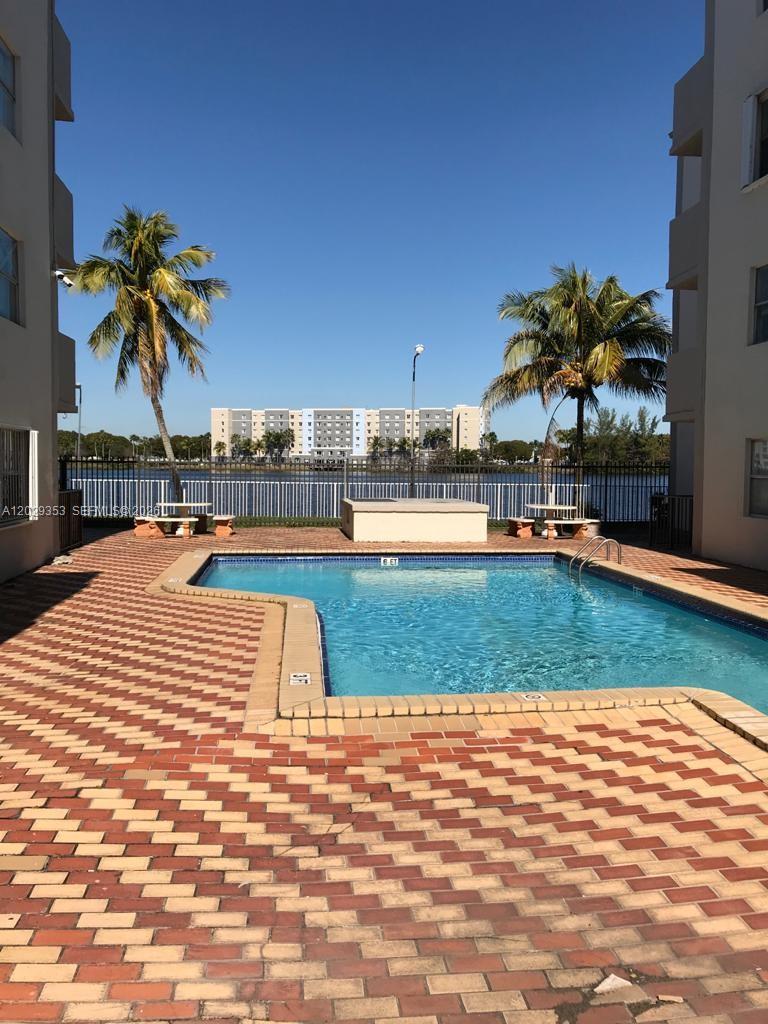 A swimming pool sits between two apartment buildings with palm trees and a lake view — 5505 NW 7th St # W417, Miami FL 33126, MIAMI, FL