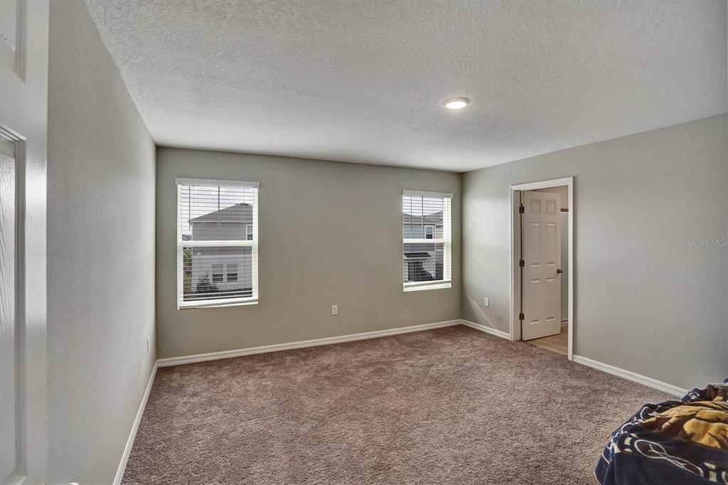 An empty bedroom with gray walls, brown carpet, two windows, and an open doorway — 4903 MAINSAIL STREET, HAINES CITY, FL