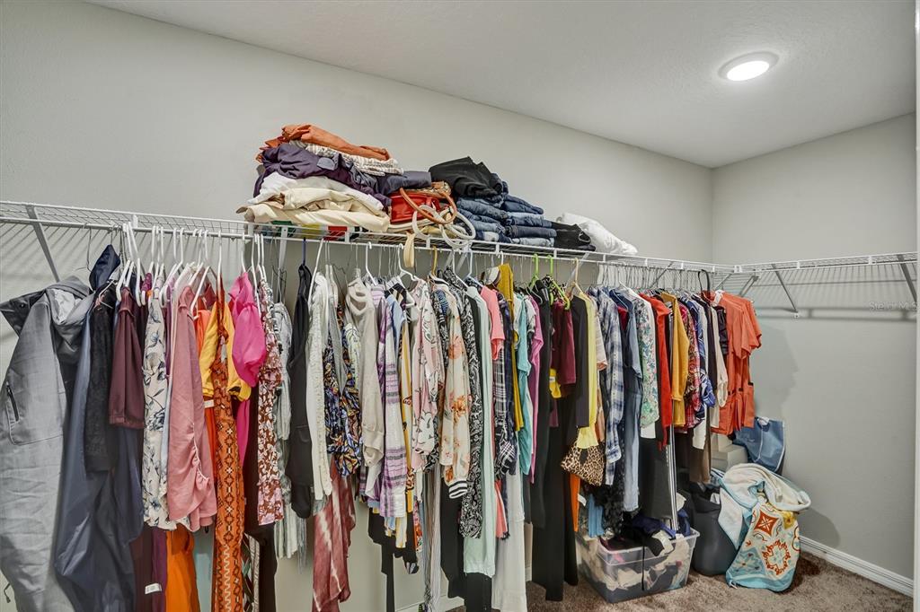A walk-in closet features white wire shelving filled with hanging clothes and folded items — 4903 MAINSAIL STREET, HAINES CITY, FL