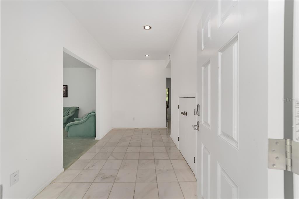 A bright entryway with white walls, recessed lighting, and light-colored tile flooring leads indoors — 6407 NW 132ND STREET, GAINESVILLE, FL