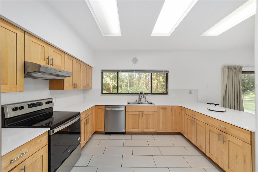 A kitchen features light wood cabinets, white countertops, stainless steel appliances, and tile flooring — 6407 NW 132ND STREET, GAINESVILLE, FL