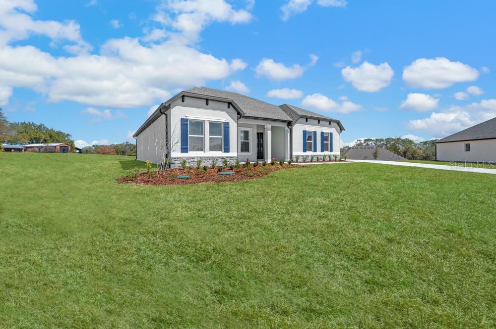 A single-story house with white stucco walls, blue shutters, and a stone-accented base — 3840 SADDLE HILL TRAIL, FRUITLAND PARK, FL