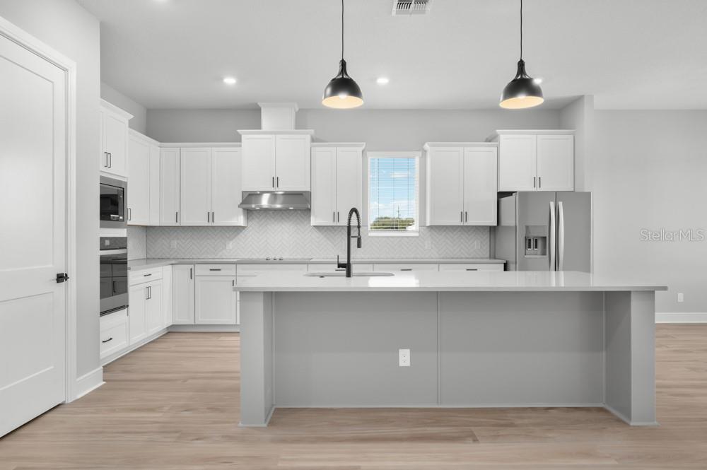 A modern kitchen features white cabinetry, a large gray island, stainless appliances, and light flooring — 3840 SADDLE HILL TRAIL, FRUITLAND PARK, FL