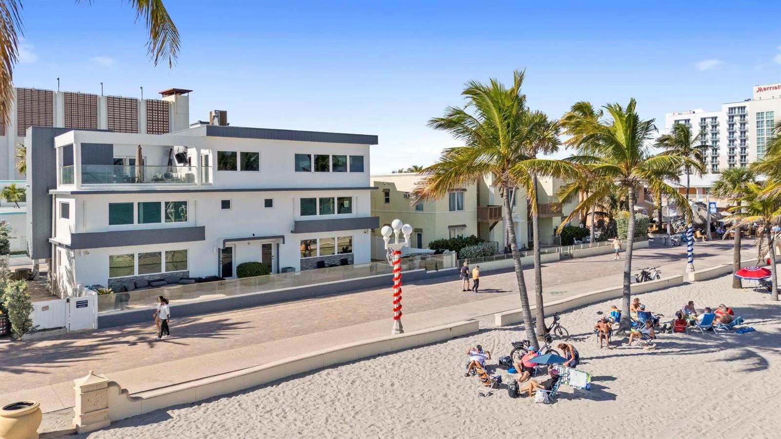 A modern white multi-story house sits along a paved boardwalk next to a sandy beach — 2203 N Surf Road, Hollywood FL 33019, HOLLYWOOD, FL