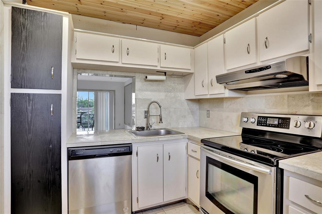 A kitchen features white cabinets, stainless steel appliances, tile countertops, and a wood-paneled ceiling — 4311 Crystal Lake Drive # 421, Pompano Beach FL 33064, POMPANO BEACH, FL