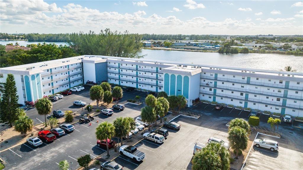 An aerial view shows a multi-story apartment building with a parking lot and a lake — 4311 Crystal Lake Drive # 421, Pompano Beach FL 33064, POMPANO BEACH, FL