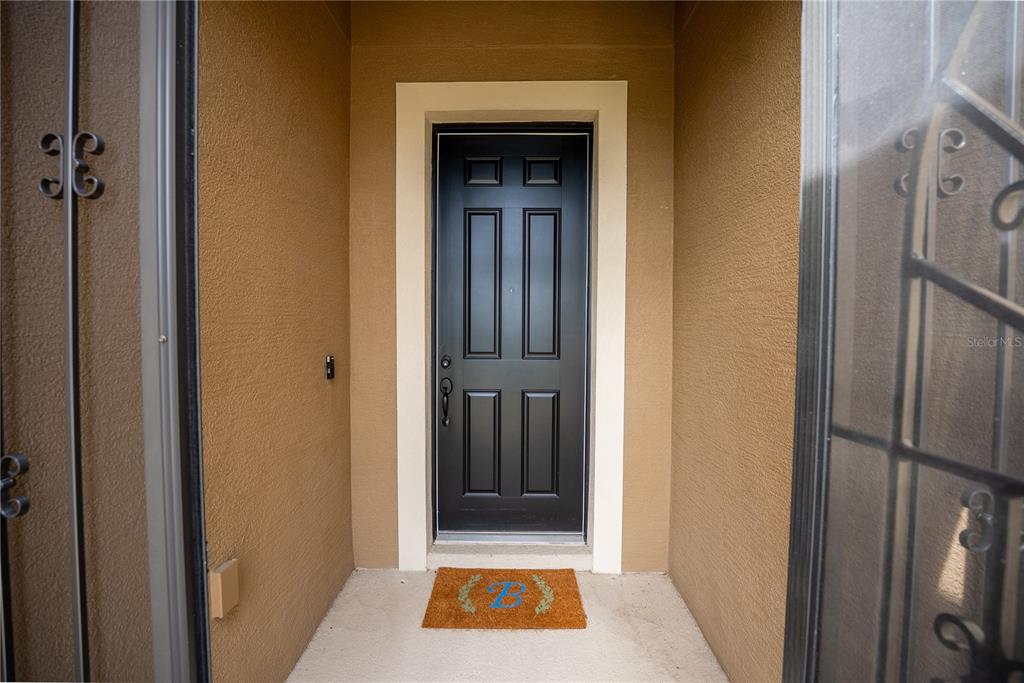 A black front door with a monogrammed welcome mat sits in a recessed entryway — 9576 SW 65TH PLACE, OCALA, FL