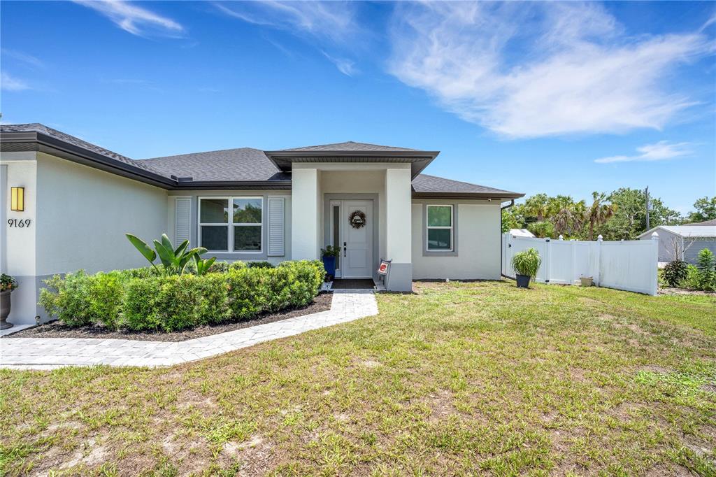 A single-story house with a light-colored exterior, a covered entryway, and a white vinyl fence — 9169 CLEWISTON TERRACE, ENGLEWOOD, FL