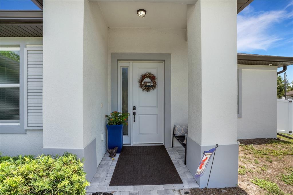 A white front door with a side window is set within a covered entryway — 9169 CLEWISTON TERRACE, ENGLEWOOD, FL