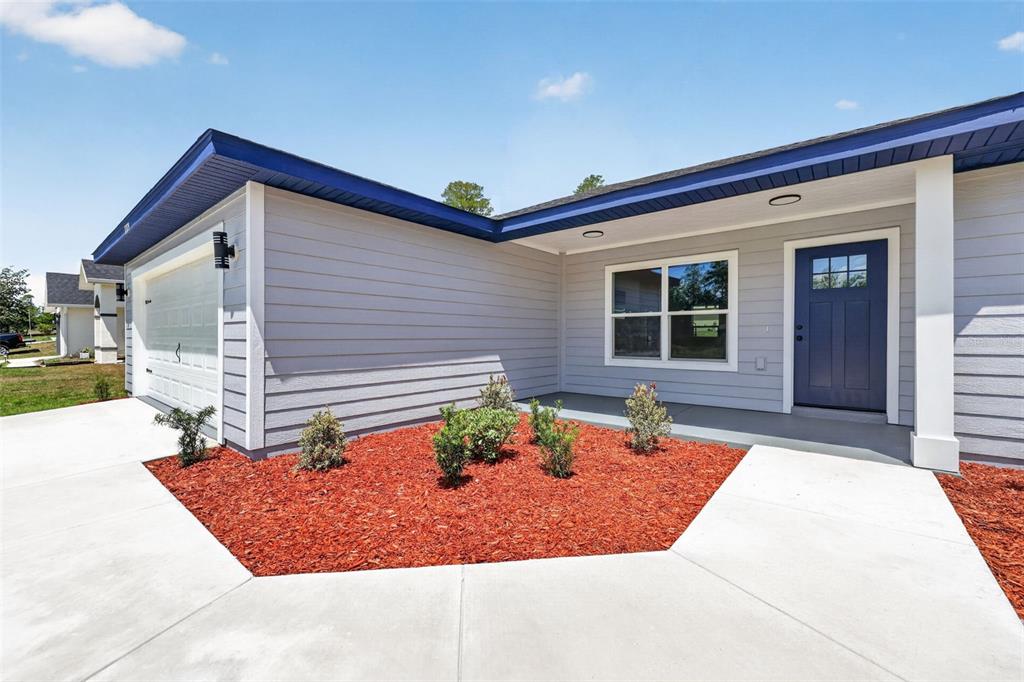 The exterior of a gray house features a blue front door and a landscaped garden — 2121 SW HILLIARD AVENUE, DUNNELLON, FL