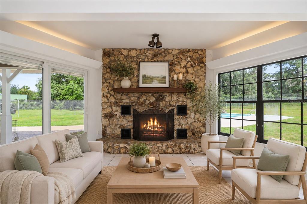 A sunroom features a stone fireplace, light-colored furniture, and large windows overlooking a backyard pool — 2809 NE 49TH STREET, OCALA, FL