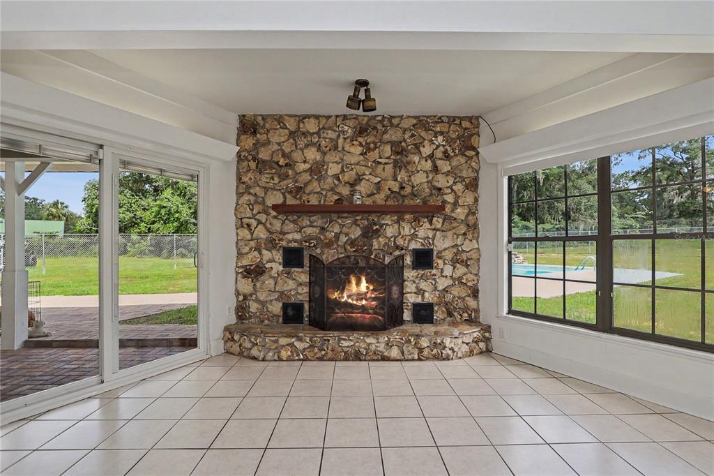 A sunroom features a stone fireplace, tile flooring, and large windows overlooking a backyard pool — 2809 NE 49TH STREET, OCALA, FL