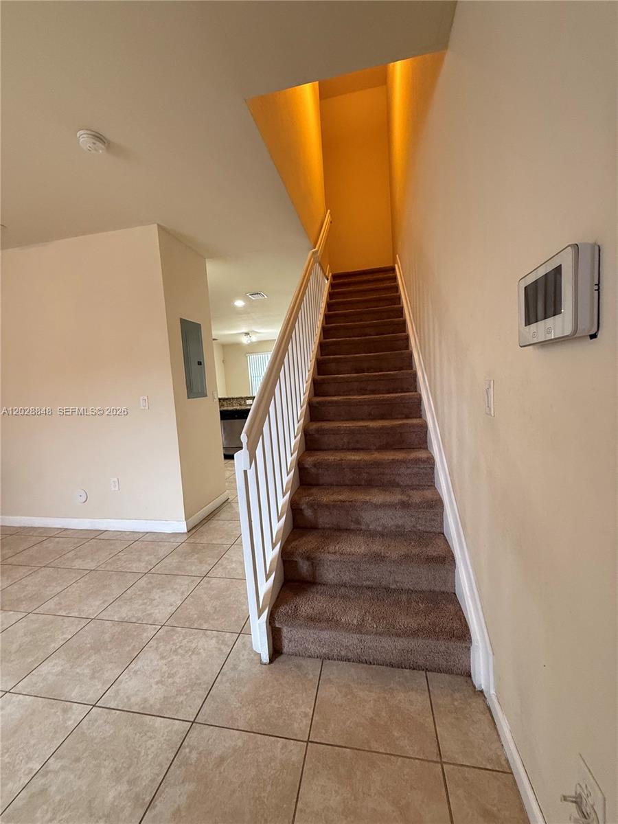 A carpeted staircase with a white railing leads to an upper level in this home — 8923 W 35th Ave, Hialeah FL 33018, HIALEAH, FL