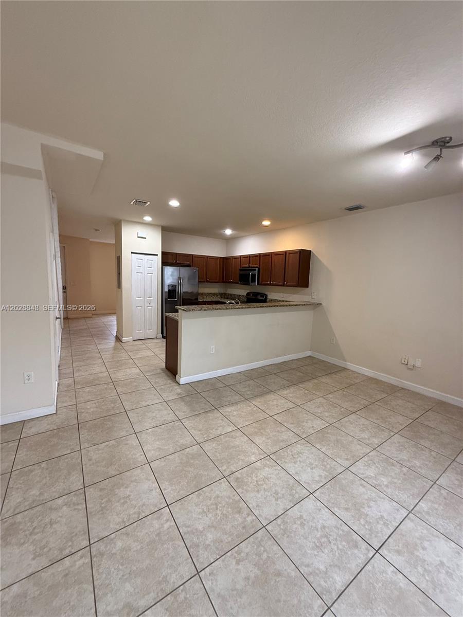 A kitchen with dark wood cabinets and granite countertops overlooks an open tiled living area — 8923 W 35th Ave, Hialeah FL 33018, HIALEAH, FL