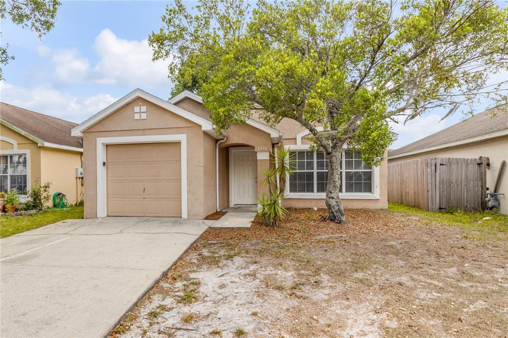 A single-story tan house with a one-car garage, a front tree, and a concrete driveway — 5546 REGAL OAK CIRCLE, ORLANDO, FL
