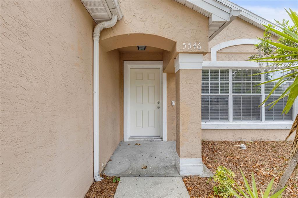 The exterior of a house features a tan stucco facade, a white front door, and a column — 5546 REGAL OAK CIRCLE, ORLANDO, FL