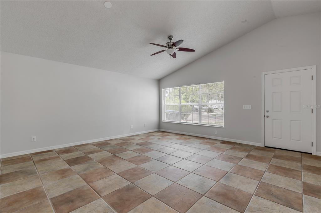 An empty room with light gray walls, a vaulted ceiling, and brown tiled flooring — 5546 REGAL OAK CIRCLE, ORLANDO, FL