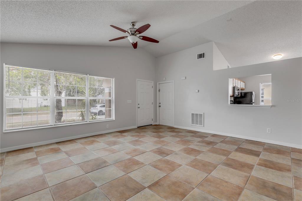 An empty living room features vaulted ceilings, a ceiling fan, tiled floors, and a pass-through window — 5546 REGAL OAK CIRCLE, ORLANDO, FL