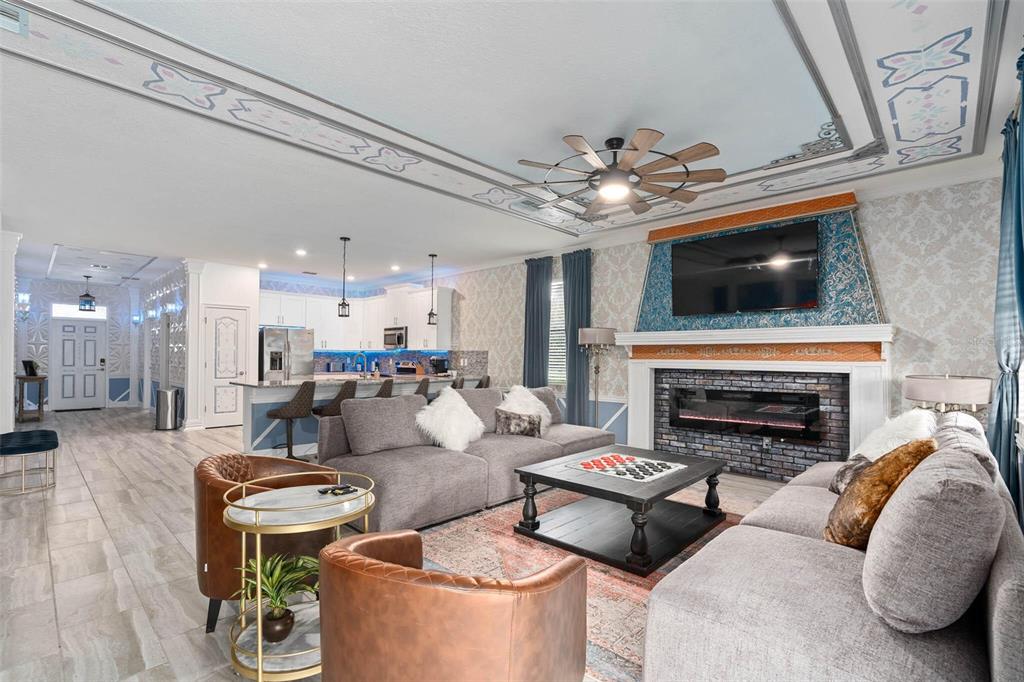A living room with a fireplace, grey sofas, brown armchairs, and an open kitchen — 1403 MOON VALLEY DRIVE, DAVENPORT, FL