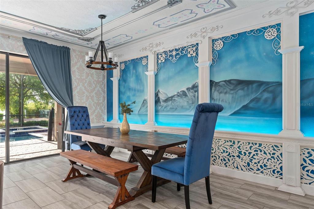 A dining room features a rustic wooden table, blue velvet chairs, and a mountain mural wall — 1403 MOON VALLEY DRIVE, DAVENPORT, FL