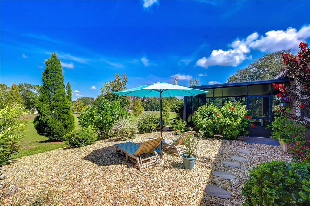 A backyard patio features two lounge chairs under a blue umbrella on a gravel surface — 10405 TREE SKYLARK PLACE, RIVERVIEW, FL