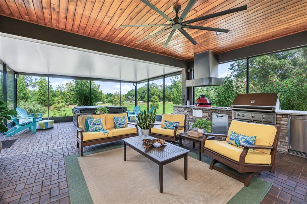 A covered outdoor patio features a stone kitchen, seating area, hot tub, and wood ceiling — 10405 TREE SKYLARK PLACE, RIVERVIEW, FL