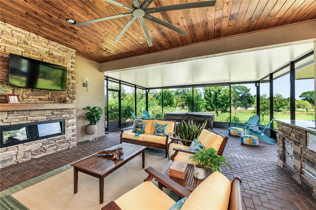 A covered outdoor patio with a stone fireplace, wood ceiling, and brick flooring — 10405 TREE SKYLARK PLACE, RIVERVIEW, FL